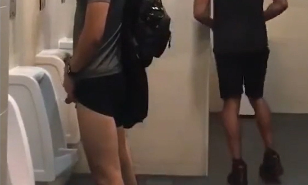 Jock pulls up shorts leg to piss at urinal